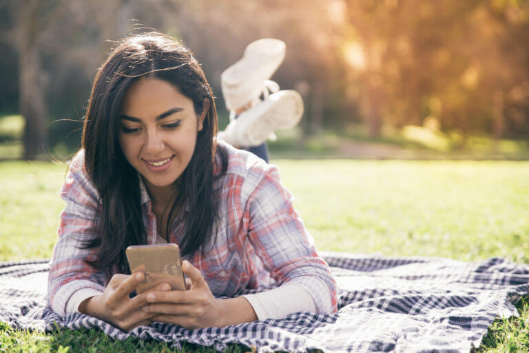 Smiling focused girl typing message on smartphone in park.