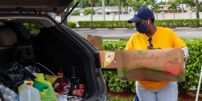 Volunteer wearing face mask loading a box of donated goods into the trunk of a car